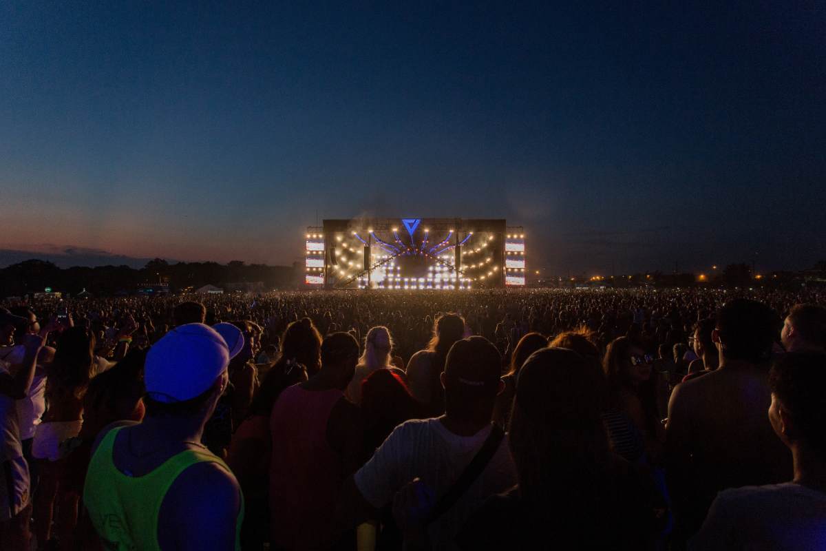Foto di un palco visto da lontano con davanti una grande folla di spalle di sera a un concerto